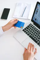 A person looking at their credit card while using their laptop